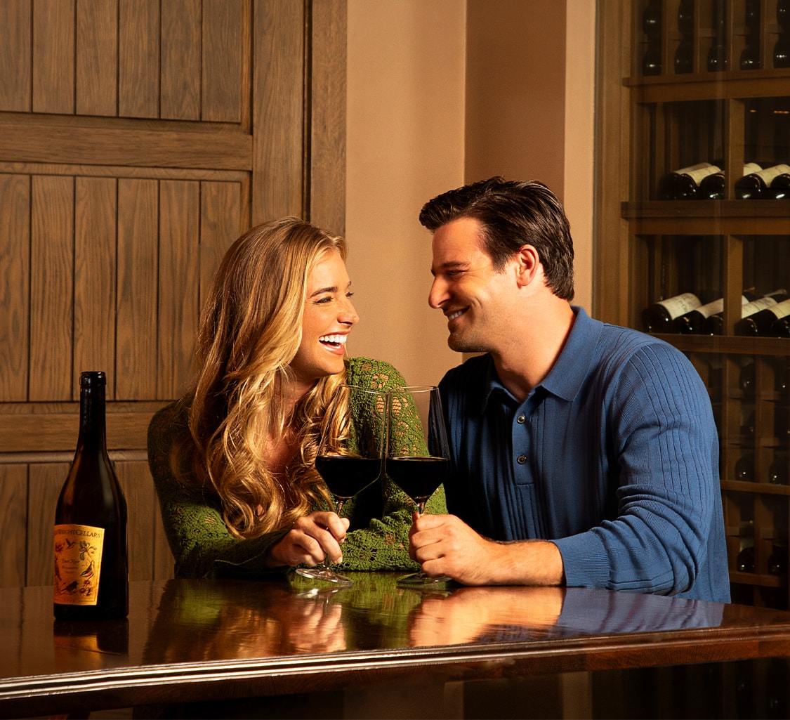 a man and a woman sitting at a table with a bottle of wine