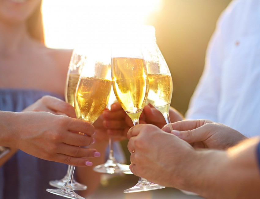 four friends clinking together their glasses of champagne and the sun setting in the background