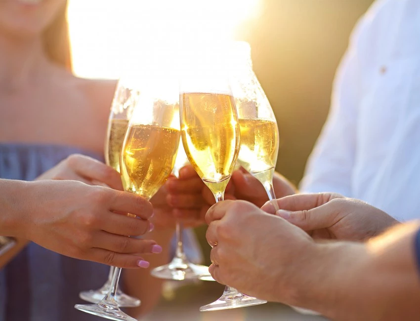 four friends clinking together their glasses of champagne and the sun setting in the background
