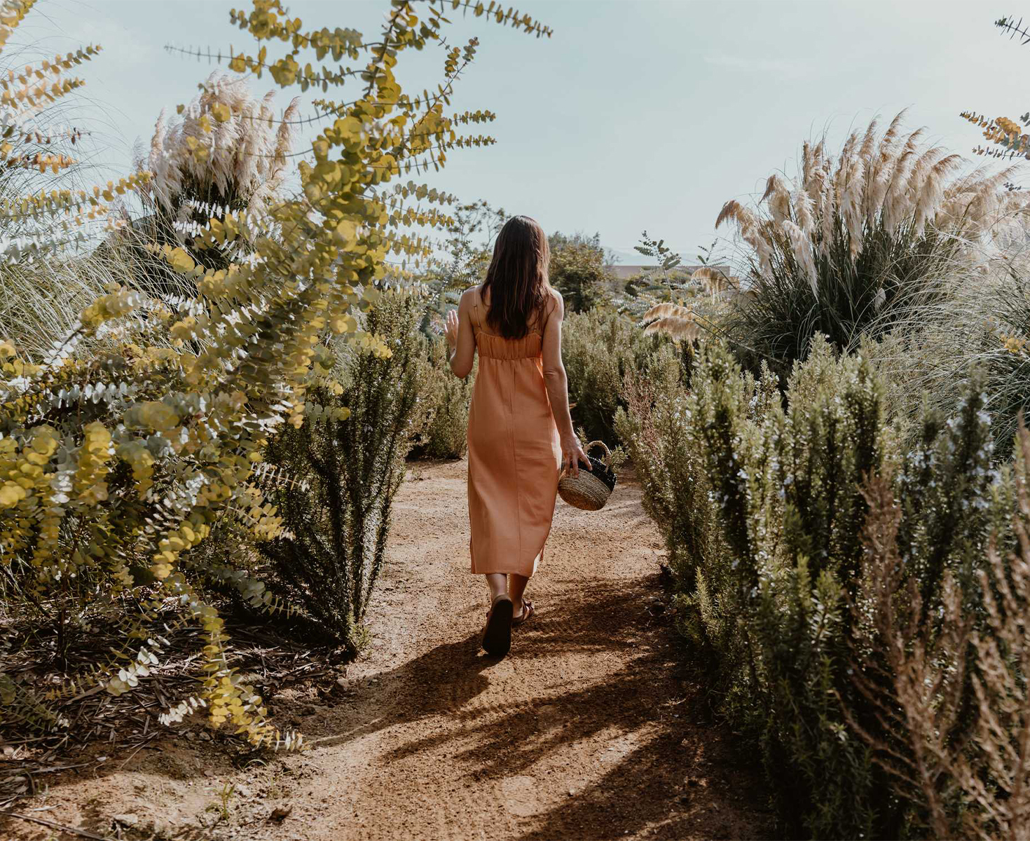 a woman walking down a dirt path with plants