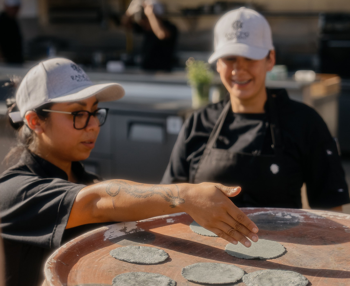 a woman in black and white hats and black aprons touching a round brown table with black circles