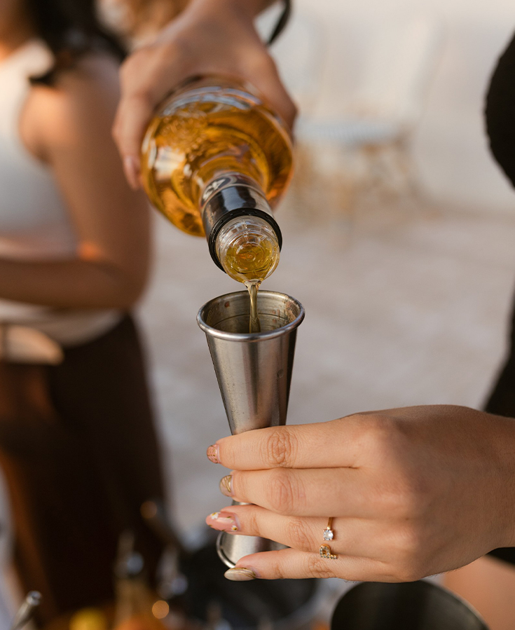 a person pouring a drink into a metal cup