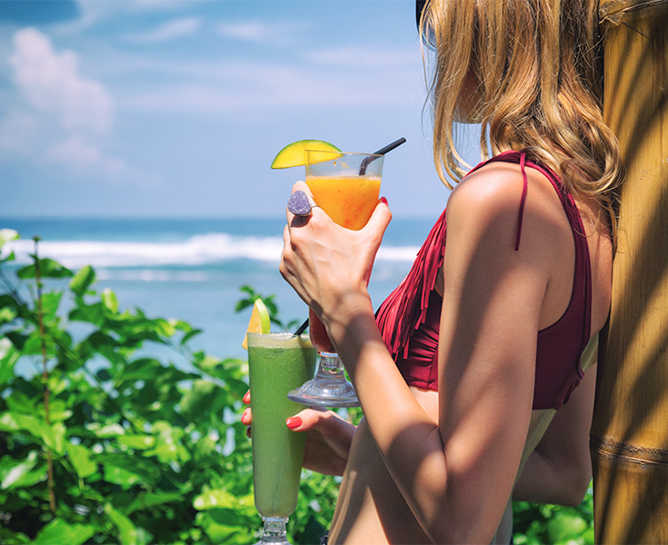 a woman wearing a red bikini and holding a frozen drink while looking at the ocean