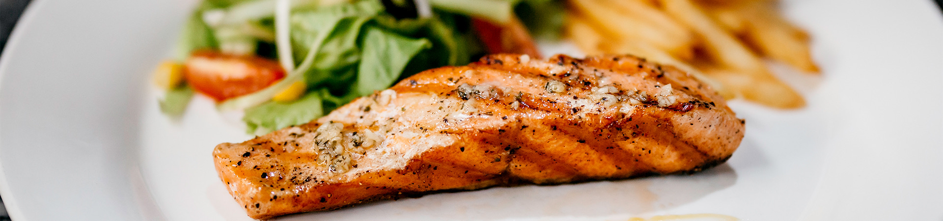 a close up of a piece of grilled salmon with mixed greens