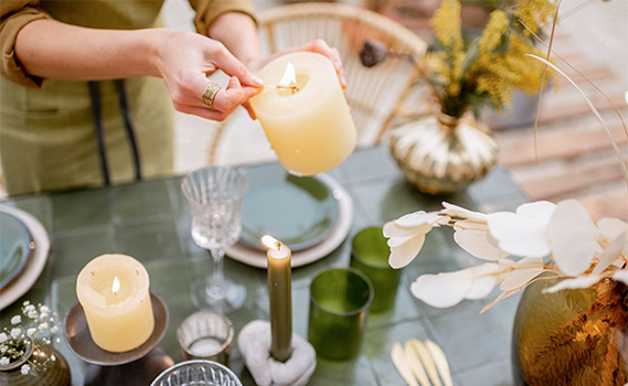 a close up of a woman lighting candles on a table set for dinner