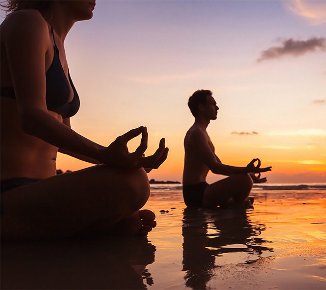 two people meditating on the beach at sunset