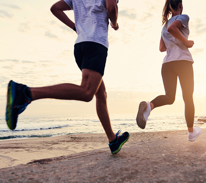 a male and a female jogging on the beach at sunset