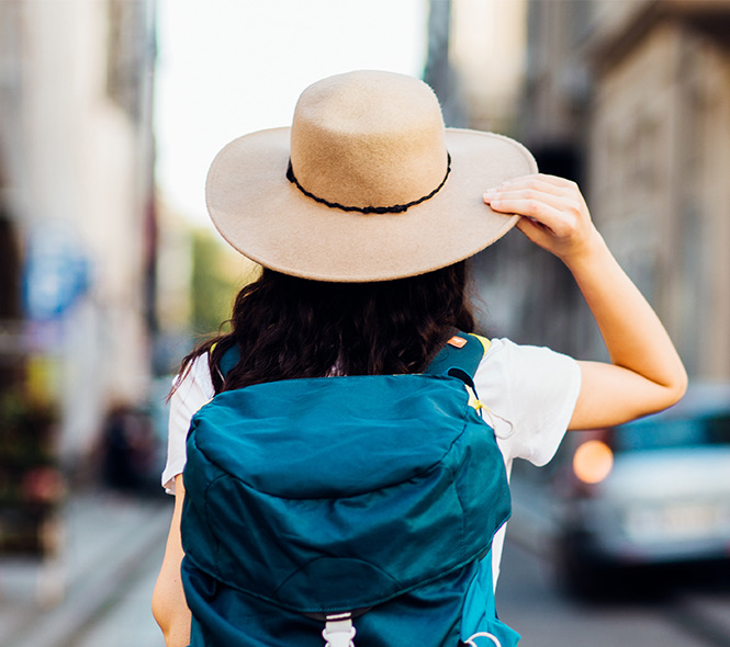 a woman wearing a blue backpack and tan hat while walking down the street