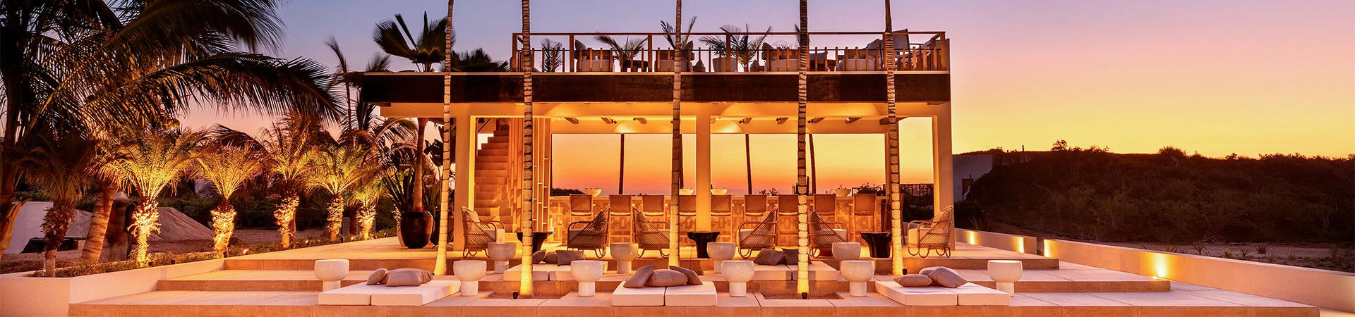 an outdoor bar and deck with palm trees at dusk
