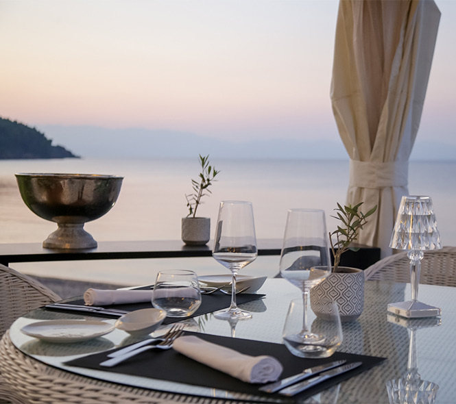 a round table with stemmed glassware and a view of the ocean at dusk