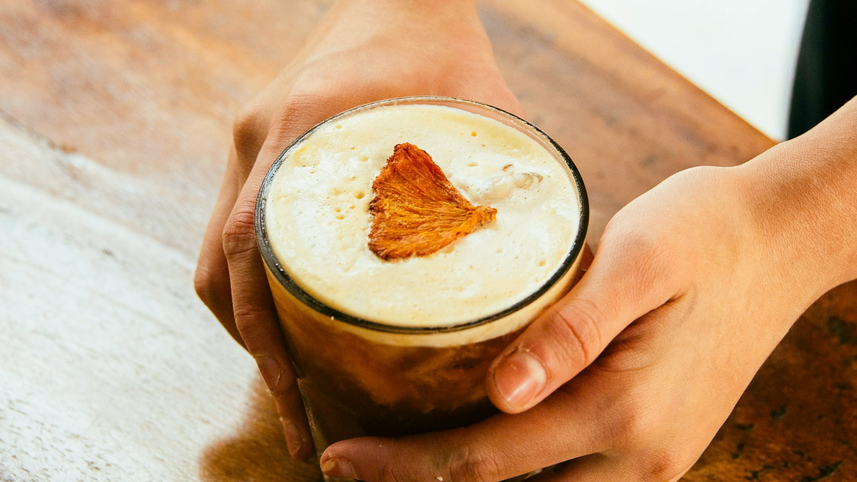 a person holding a glass of liquid with a pineapple leaf on top
