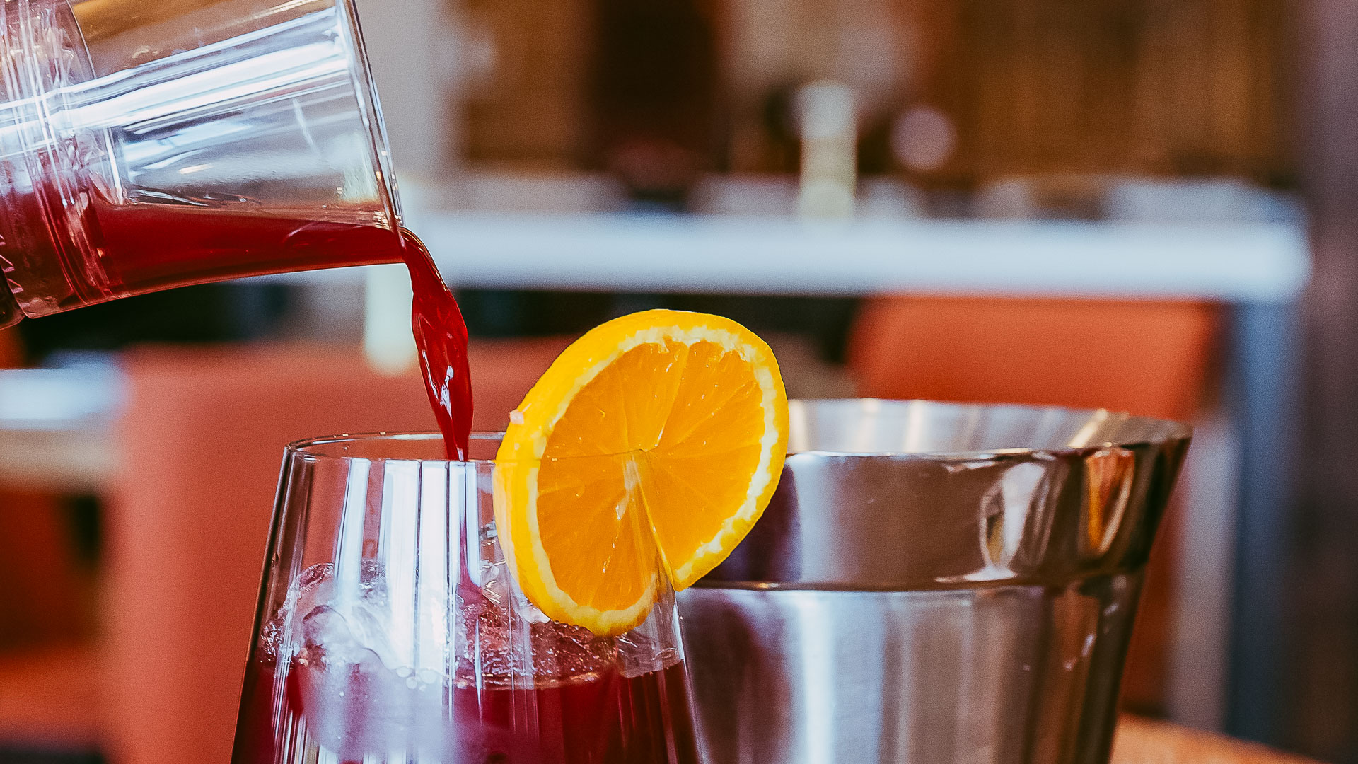 a person pouring a drink into a glass with a slice of orange