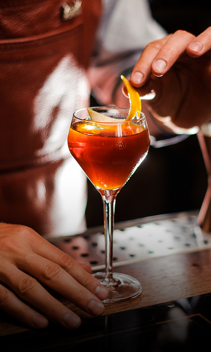 a person putting a slice of orange into a glass of liquid