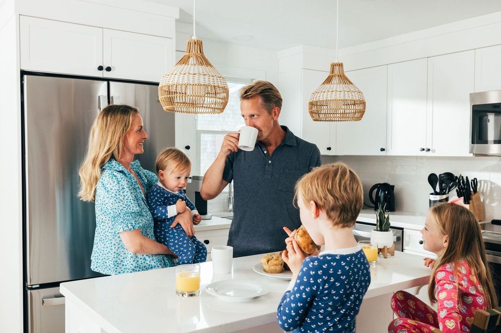 a man and woman holding a cup of coffee and two children in a kitchen