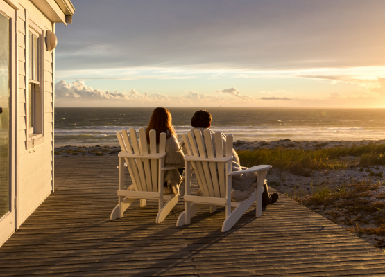 two people sitting in chairs on a deck overlooking the ocean