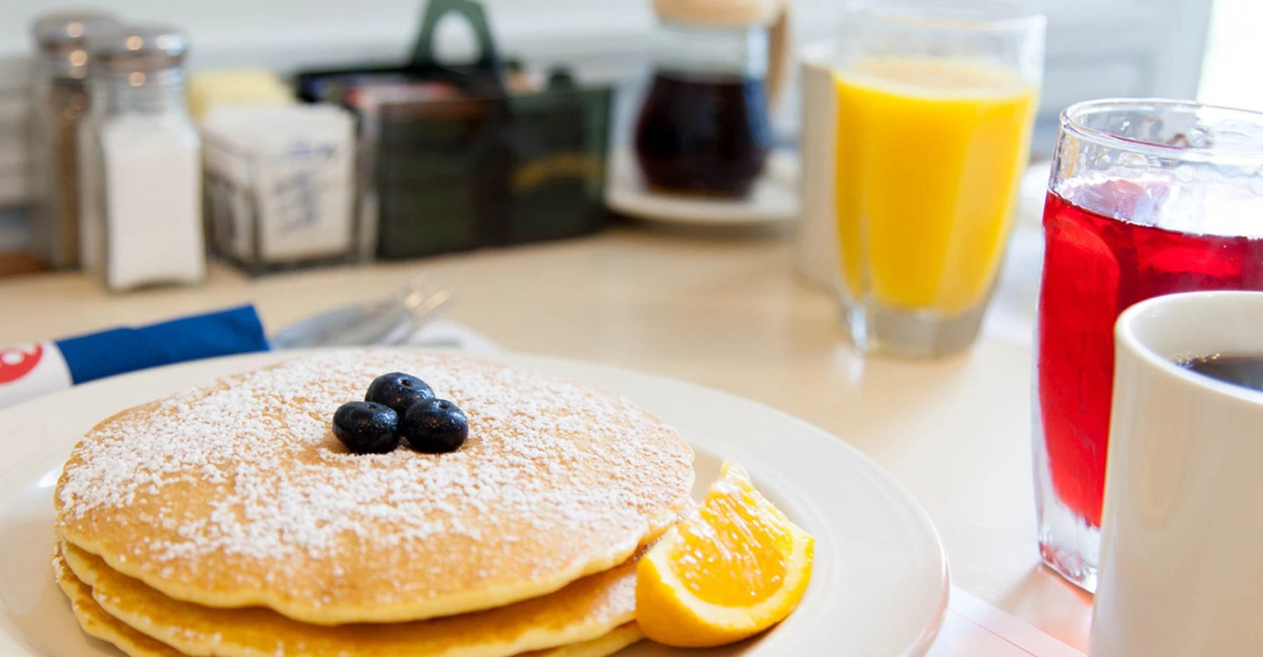 a plate of pancakes with blueberries and a slice of orange
