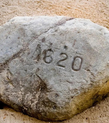 a large rock with numbers carved into it with Plymouth Rock in the background