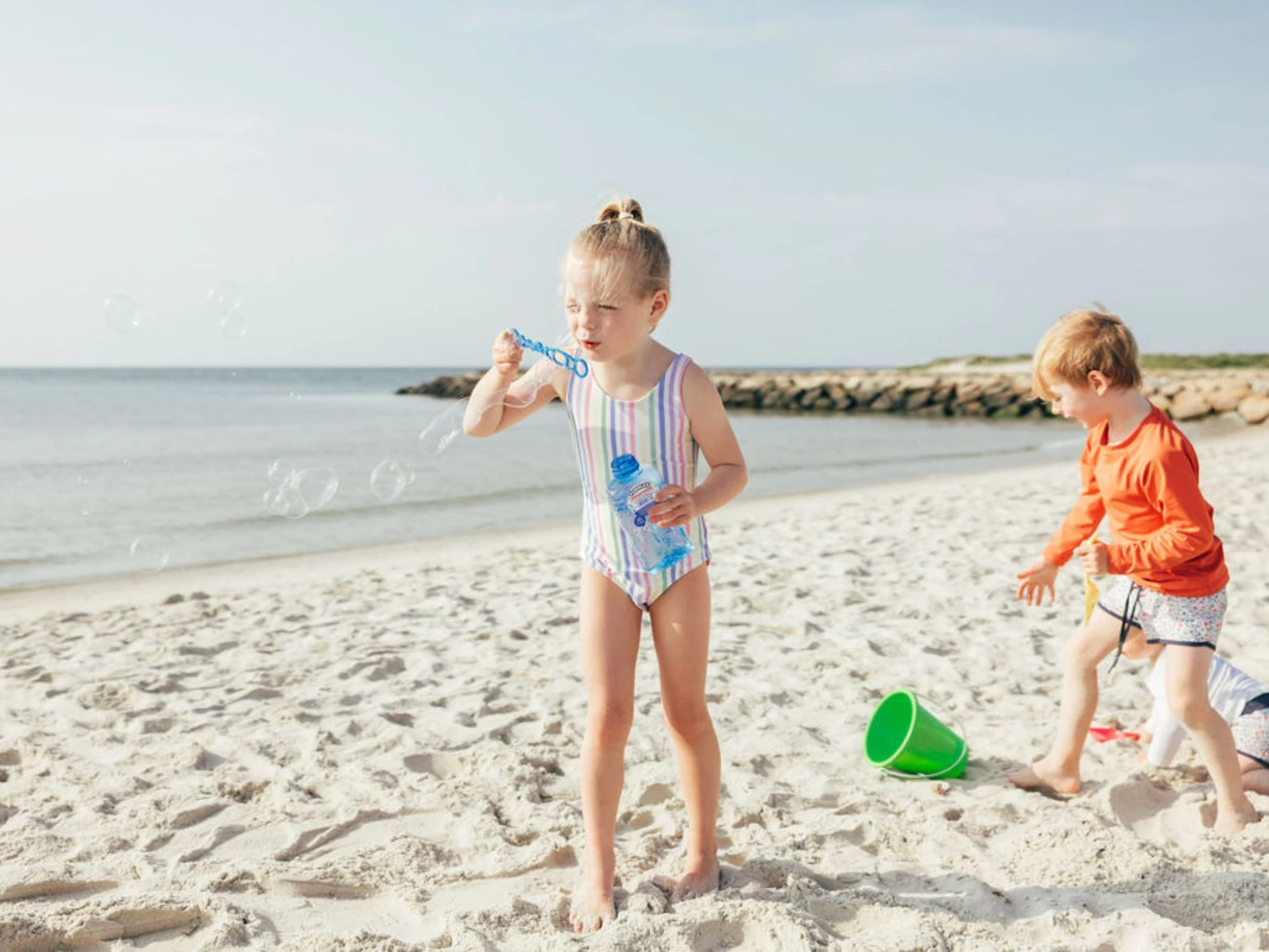 young children on the beach with a little girl blowing bubbles