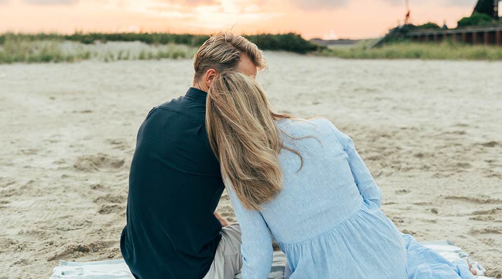 a man and woman sitting on a blanket on a beach