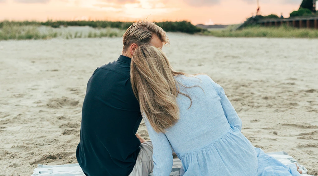 a man and woman sitting on a blanket on a beach
