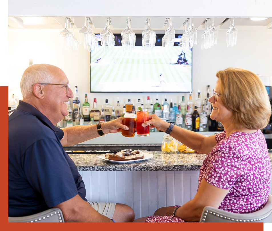 a man and woman sitting at a bar toasting with drinks