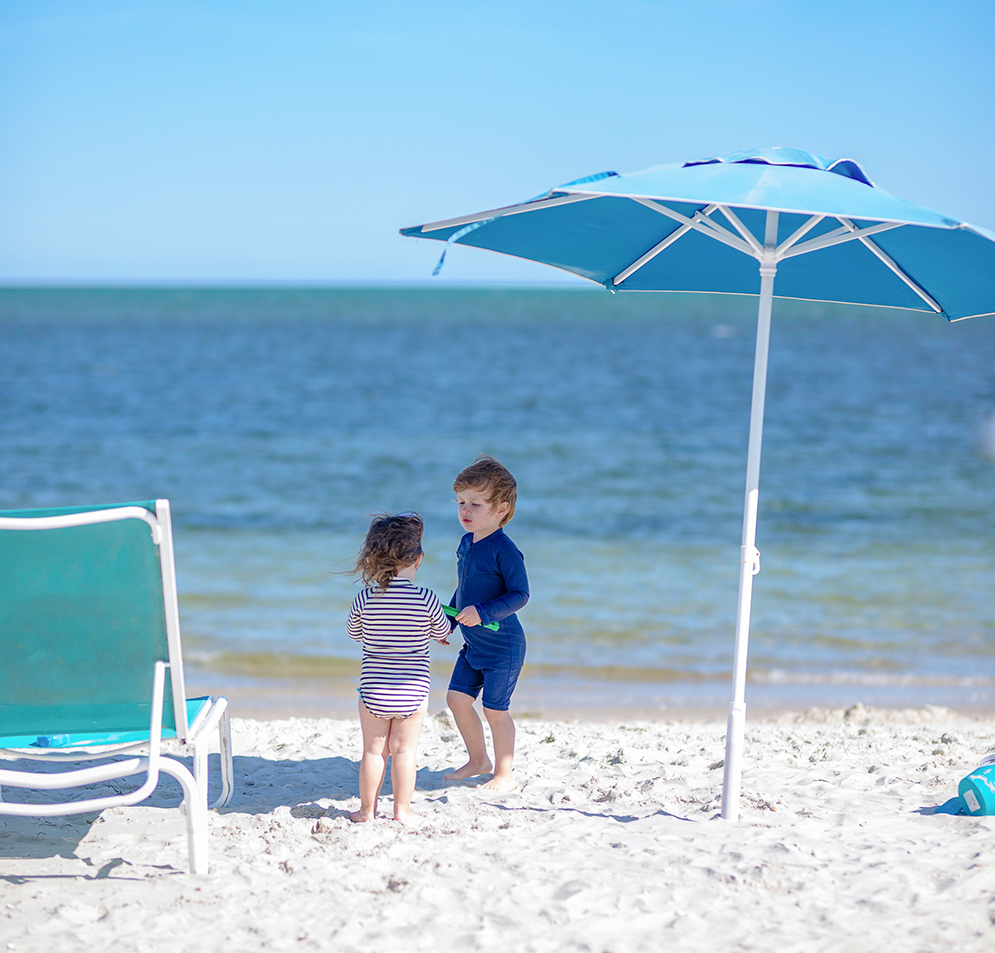a couple of children stand under an umbrella on a beach