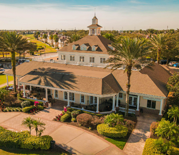Aerial view of a large building with a brown roof and white columns, surrounded by trees and a parking lot.