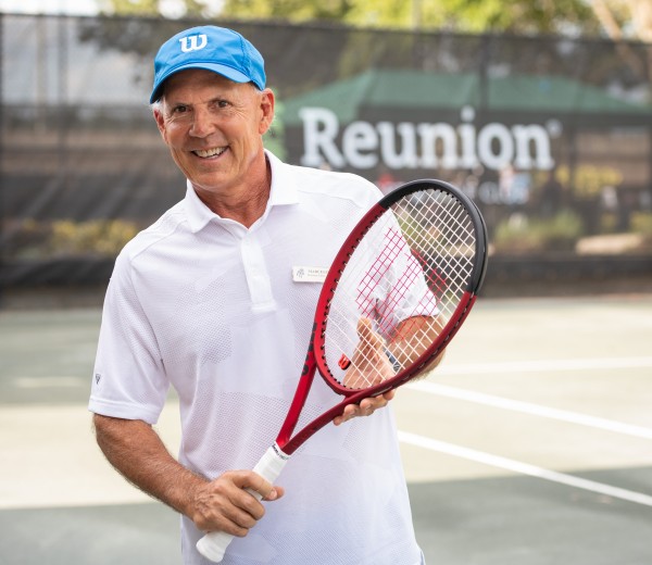 a smiling man holding a red tennis racket on the court