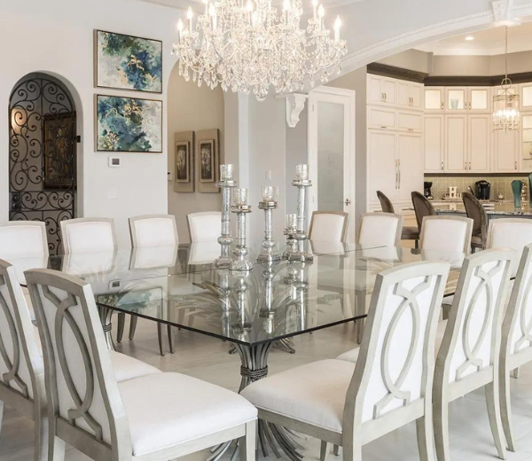 A large dining room with a glass table, white chairs, a chandelier, and candle holders.