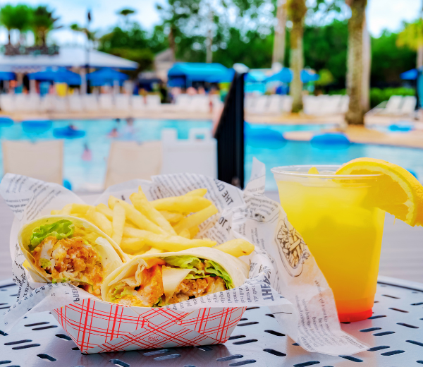A meal of wraps and fries with a drink beside a pool.