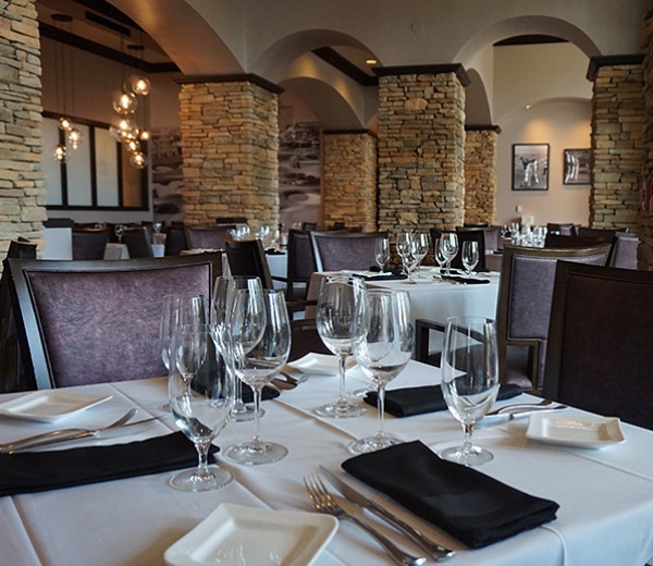 A formal dining room with tables set for dinner, stone columns, and an arched ceiling.