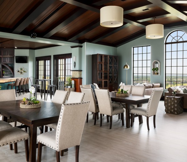 A dining area with tables and chairs, a bar, and large windows.