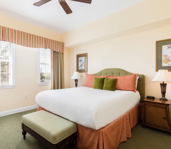 large comfortable bed with colorful accent pillows and an overhead fan