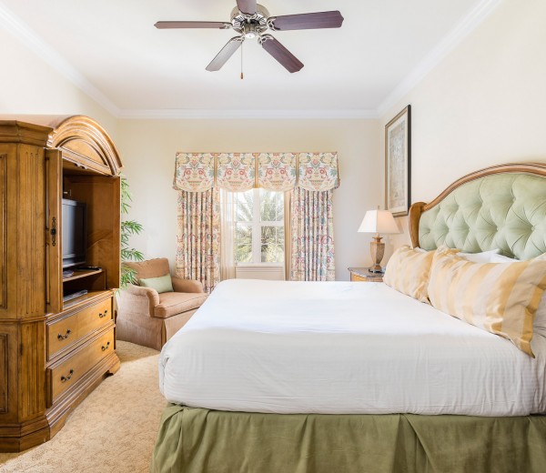 A wide view of a hotel room with a large bed, a TV, a chair, and a window.