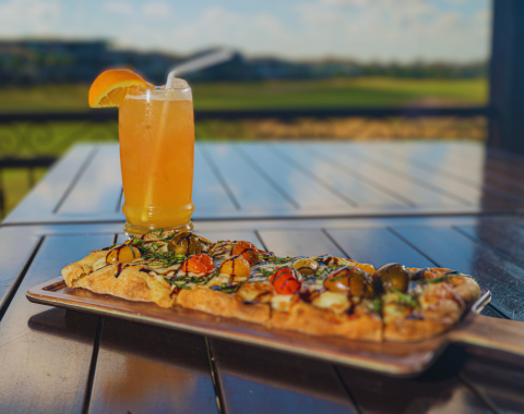 a pizza on a plate with a drink in the background