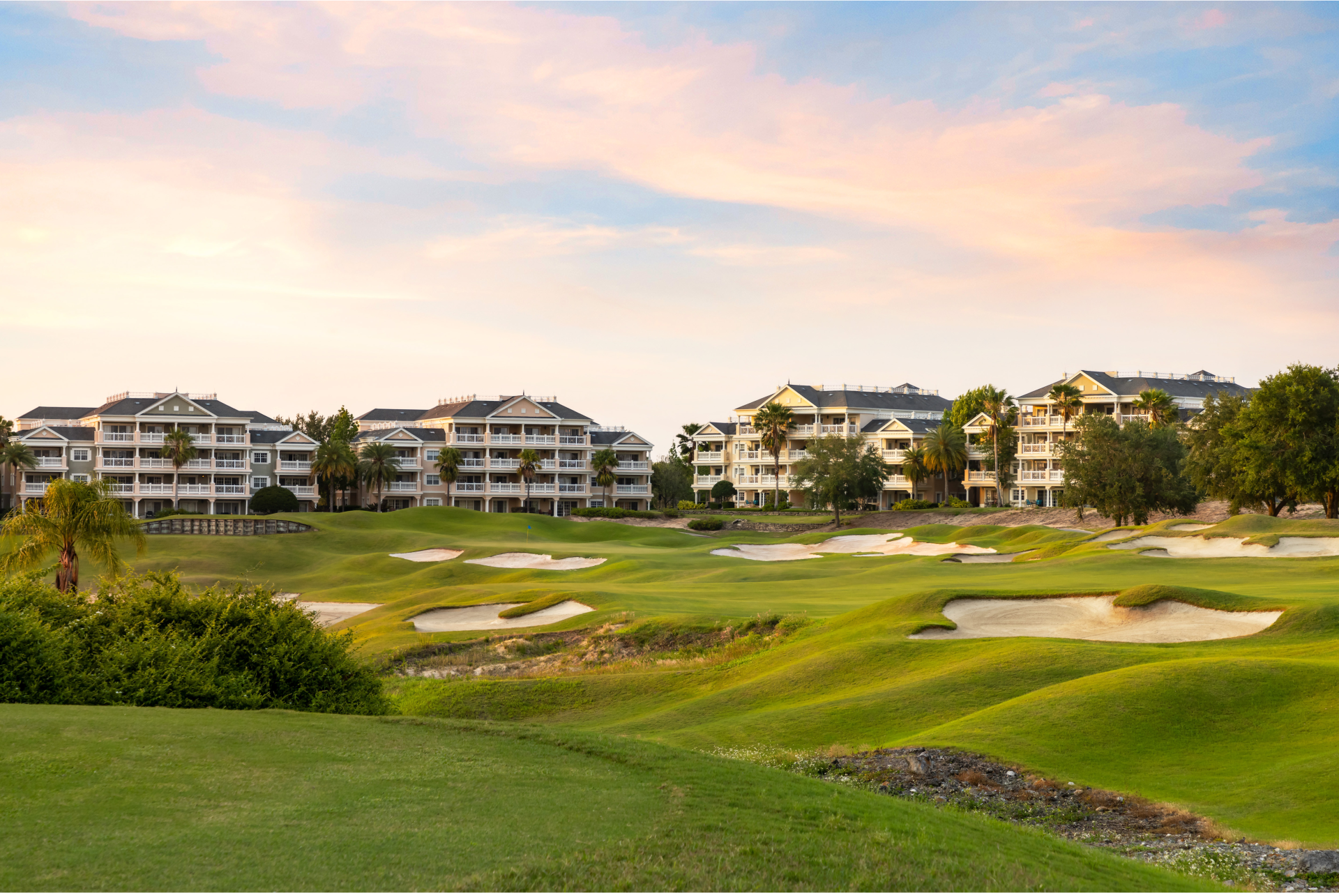 A golf course with sand traps and buildings in the background