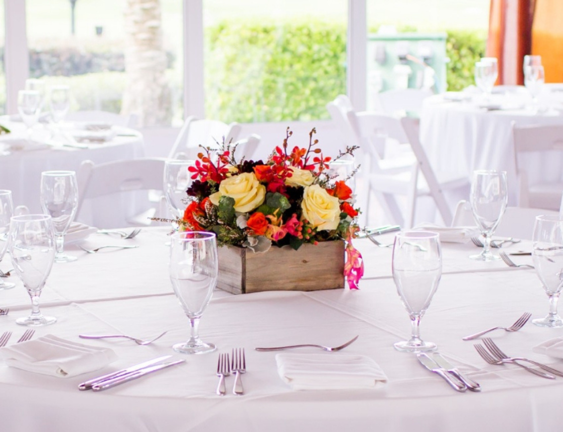 A dining table set with white tablecloth, flowers, glasses, and silverware.