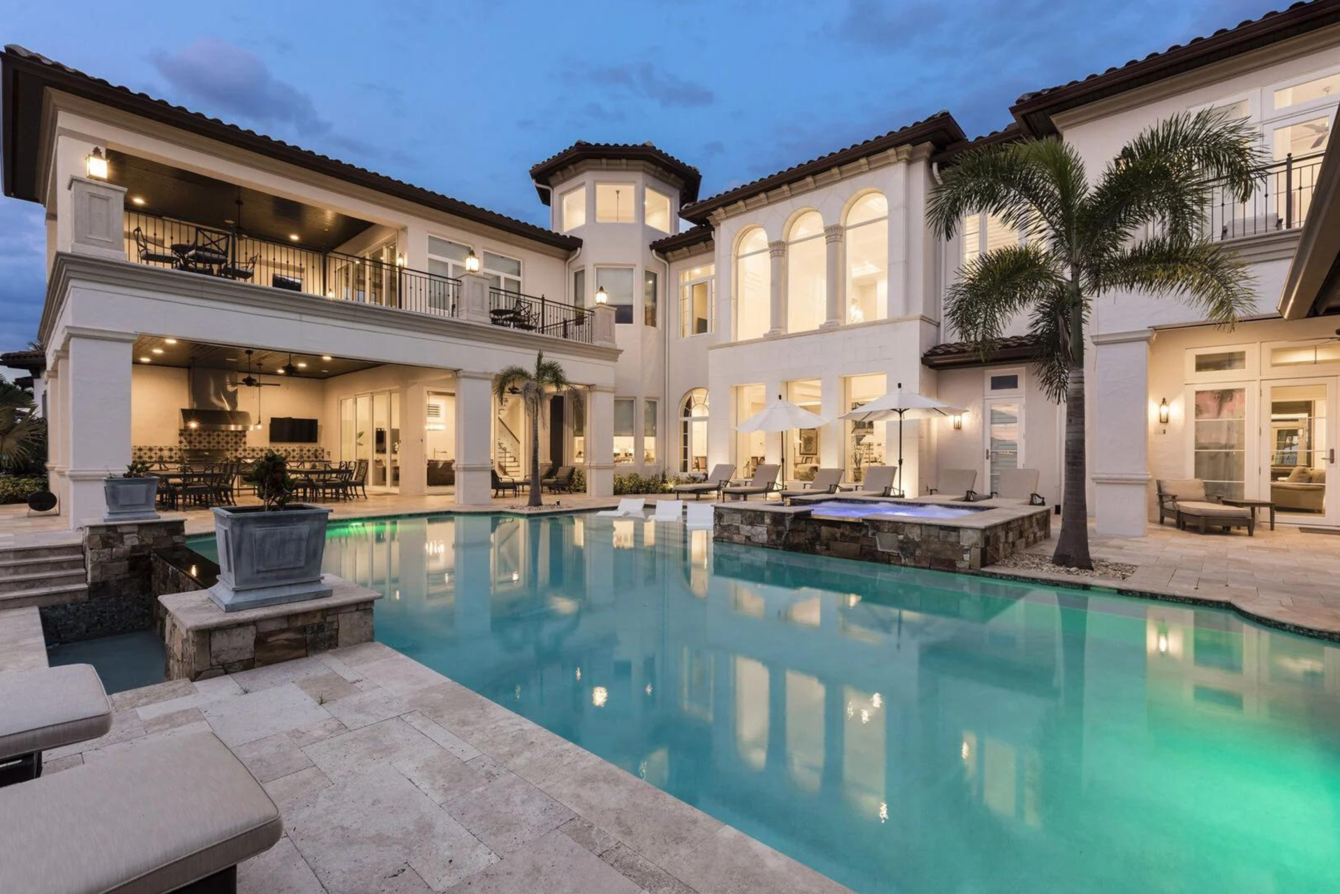A large white building with a pool and palm trees in front of it at dusk.
