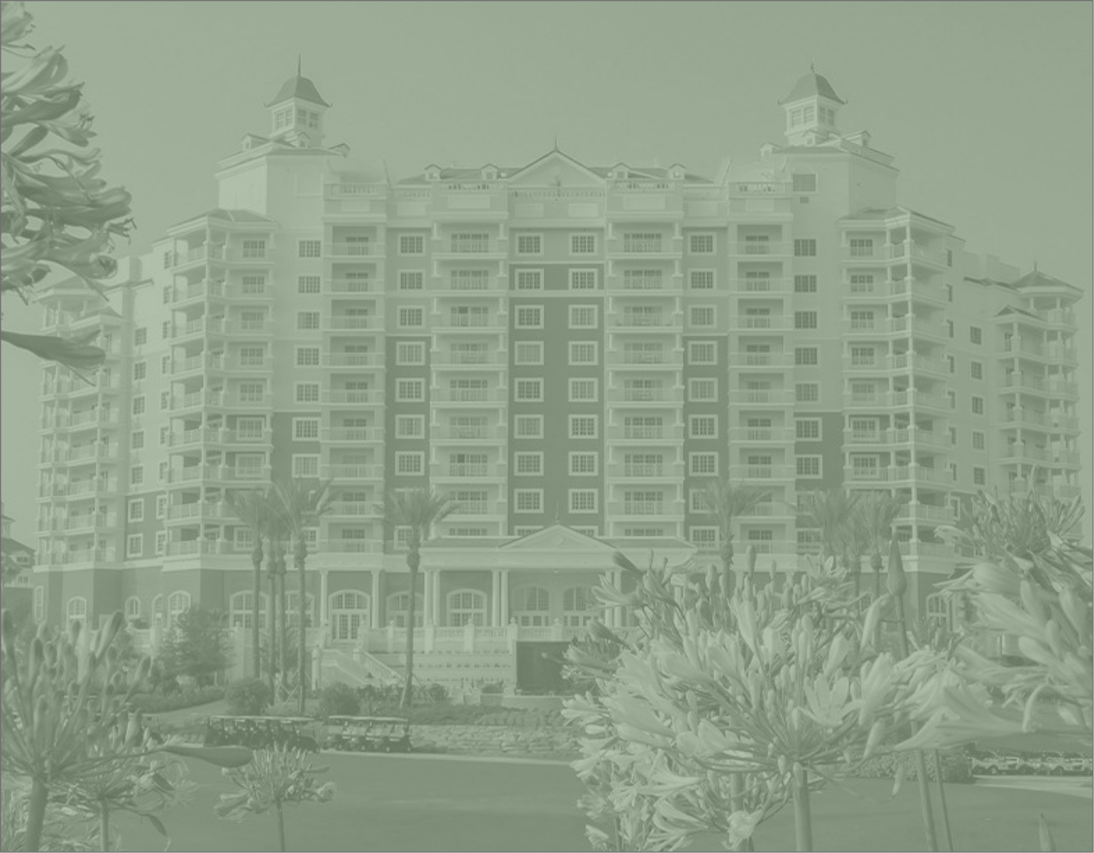 A large, multi-story building with balconies and towers, surrounded by palm trees and gardens.