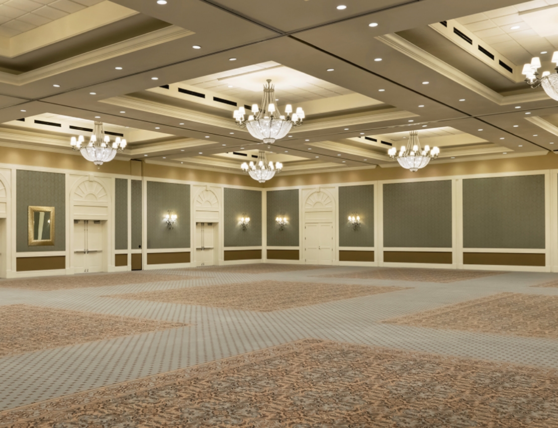 A large, empty meeting room with chandeliers, carpeted floor, and wall paneling.