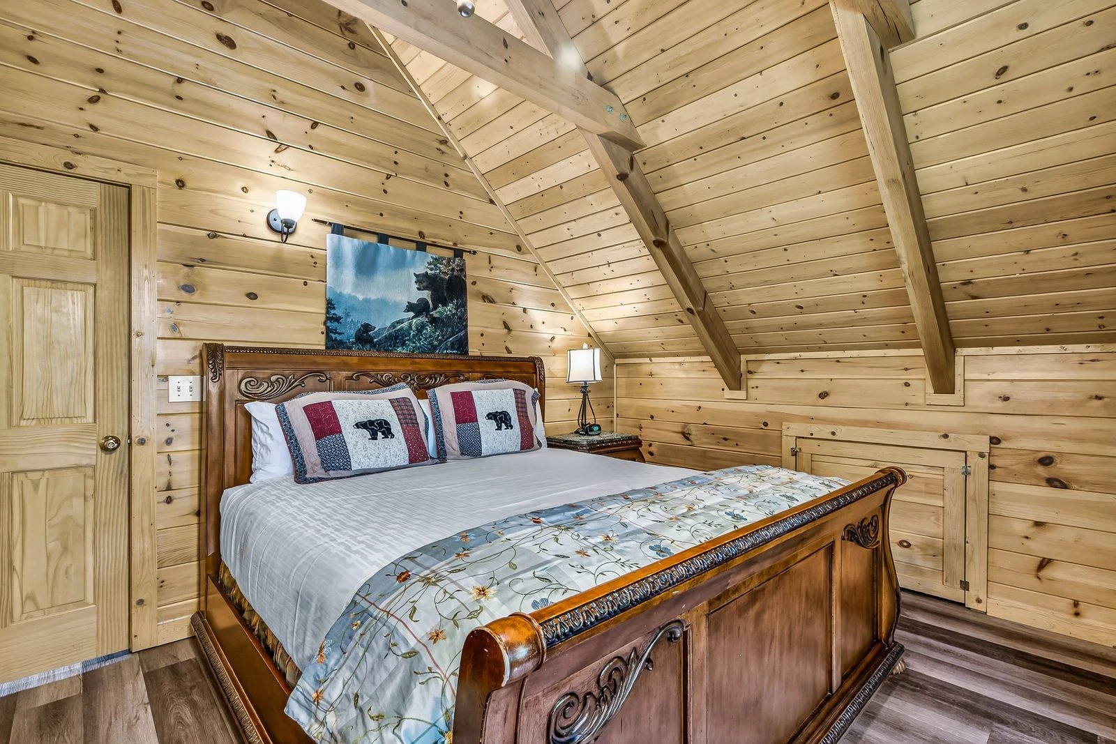 A cozy room with a large bed, wood-paneled walls, and a vaulted ceiling.