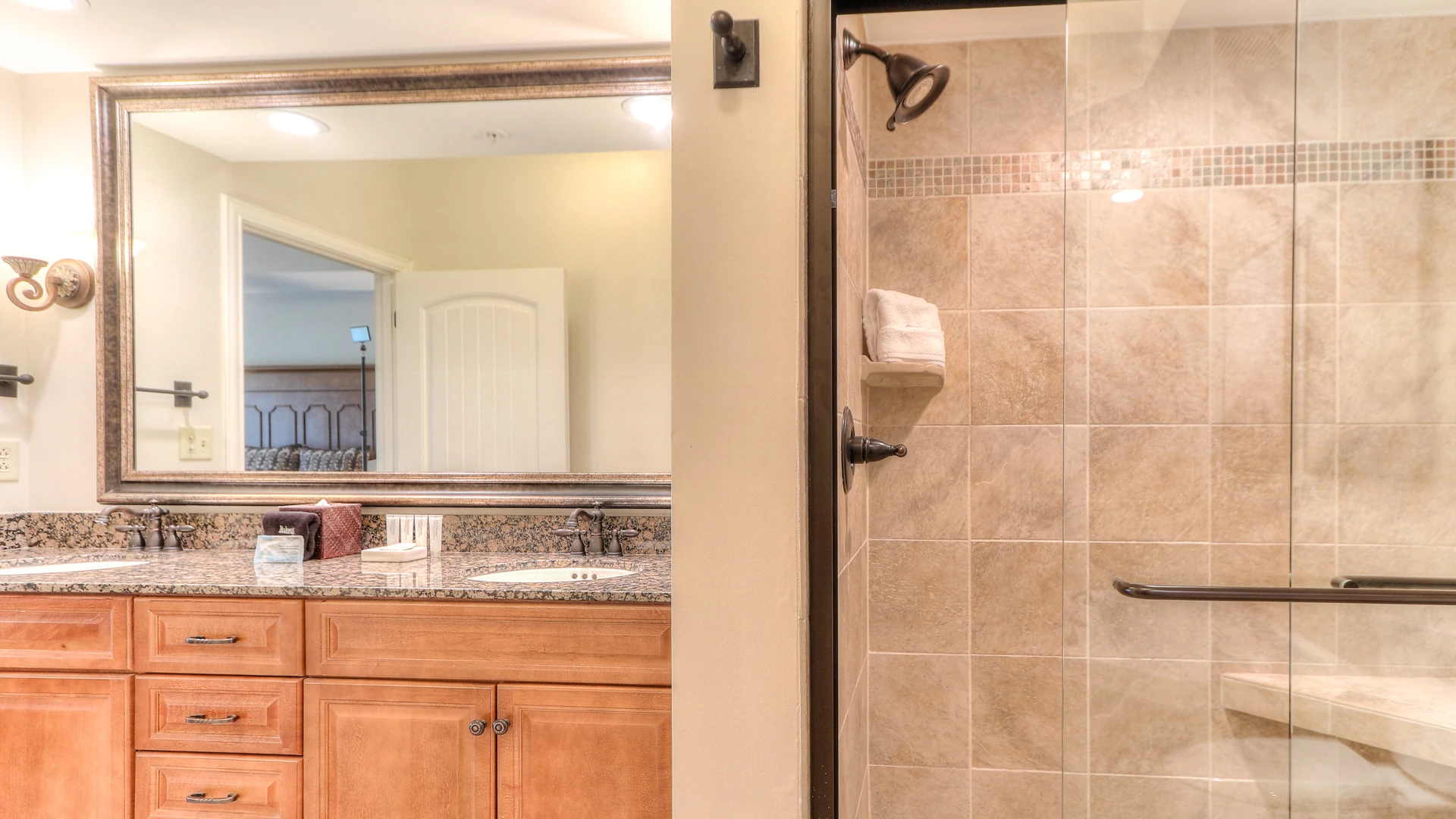 A bathroom with a granite countertop, wood cabinets, and a tiled shower.