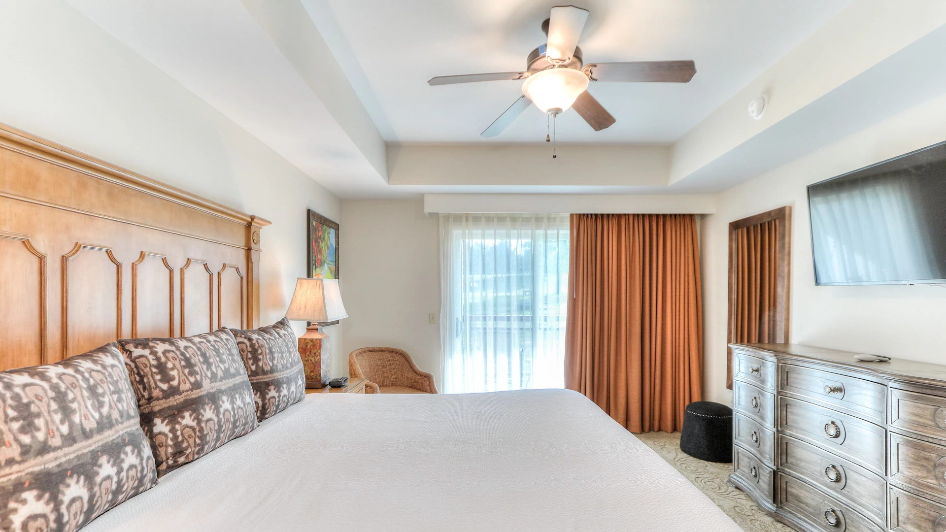 A wide view of a hotel room with a large bed, dresser, TV, and window.