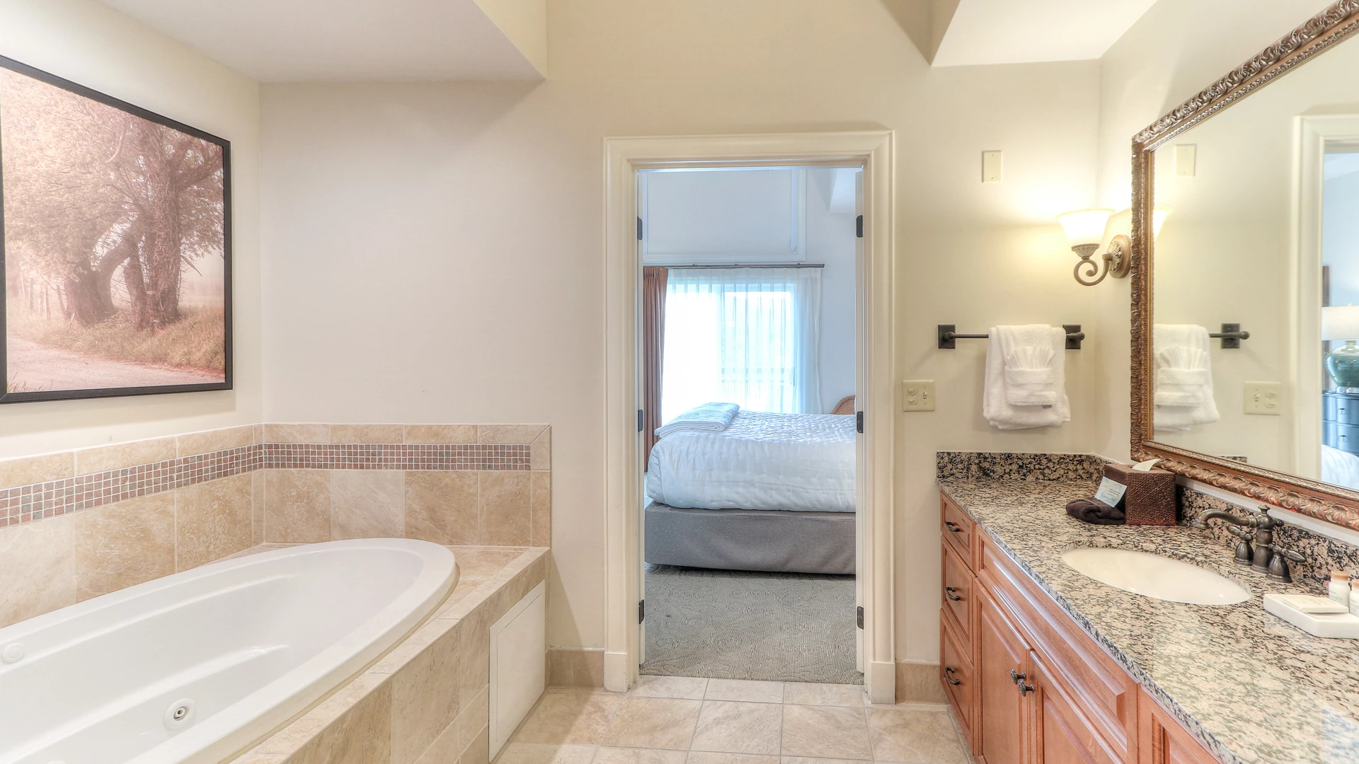 A bathroom with a soaking tub, granite countertop, and a view of the bedroom through an open doorway.