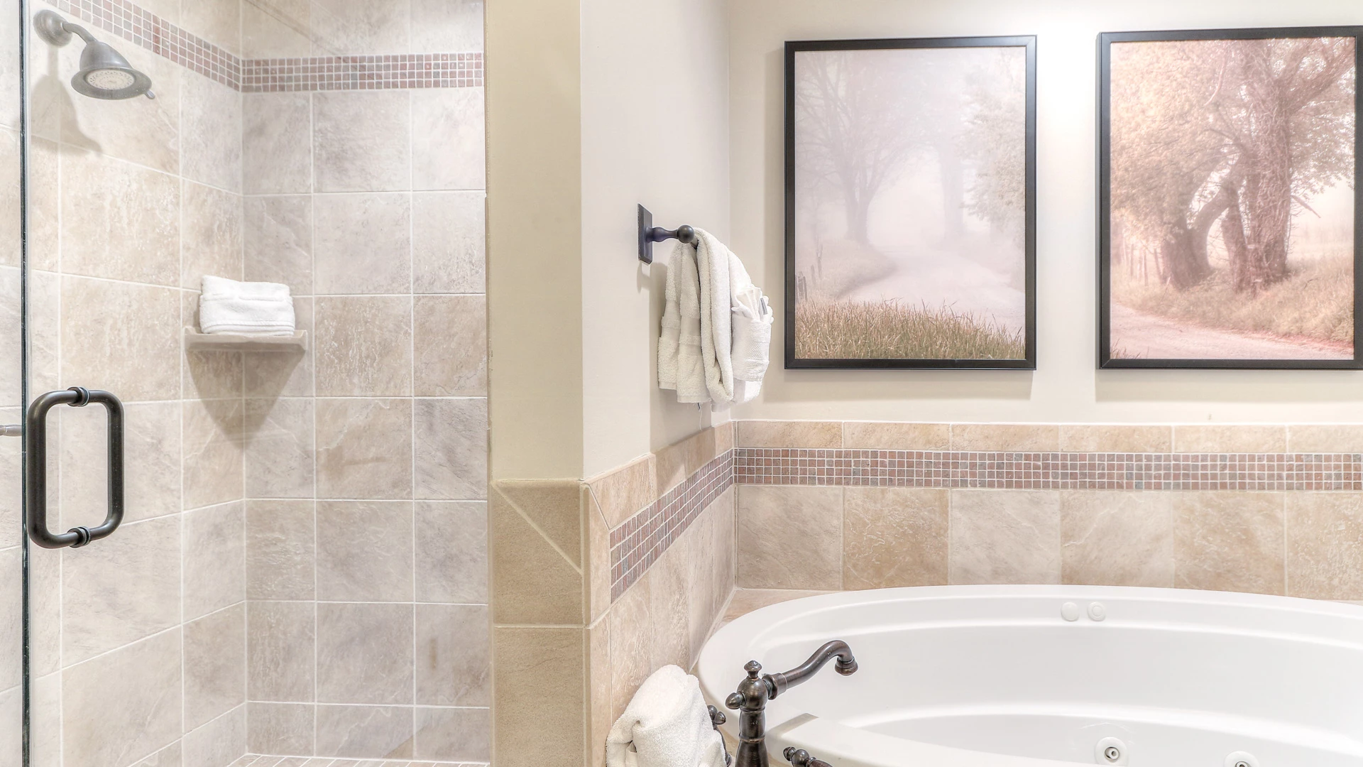 A bathroom with a shower and bathtub, tiled walls, towels, and two pictures on the wall.
