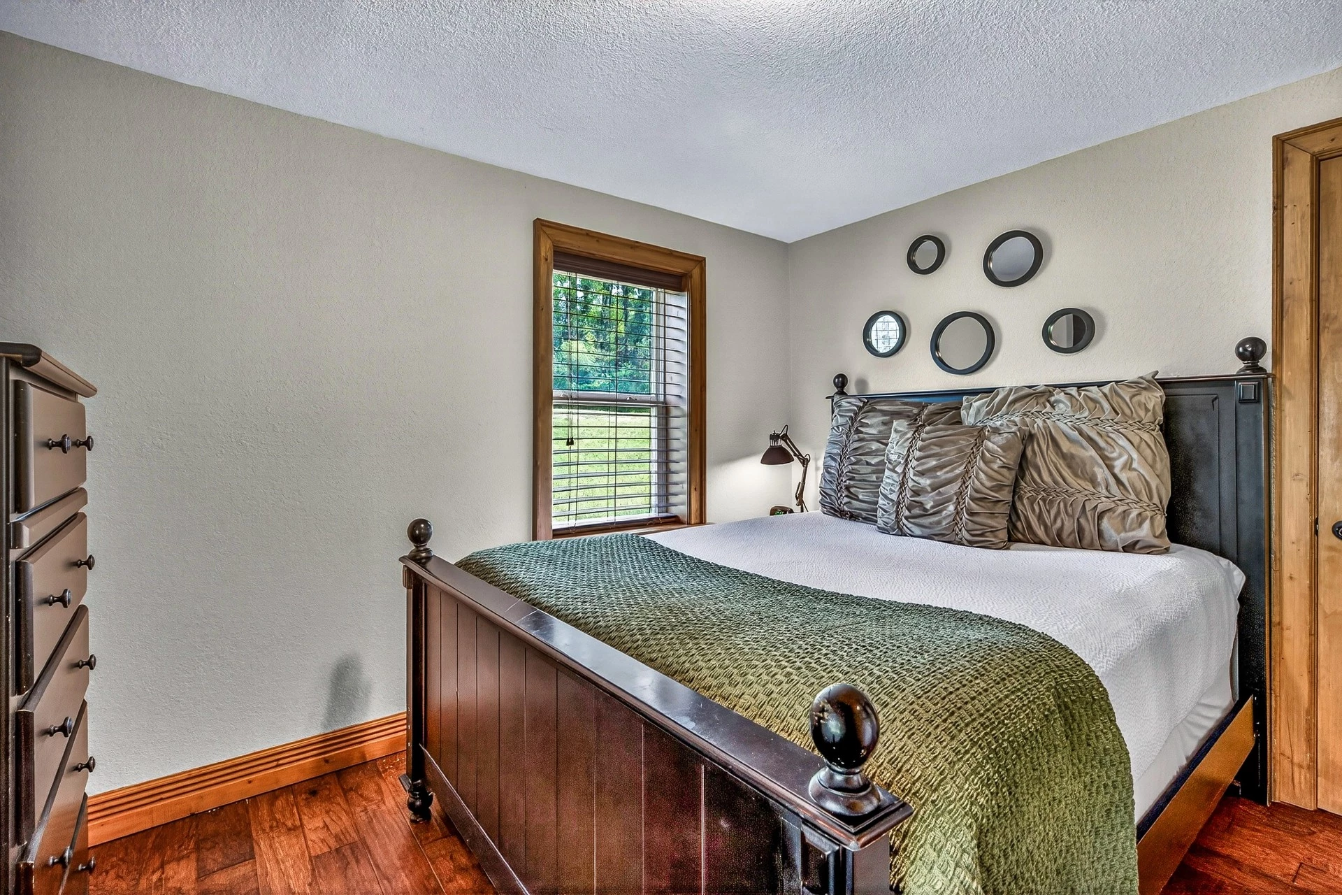 A bedroom with a bed, window, dresser, and mirrors.