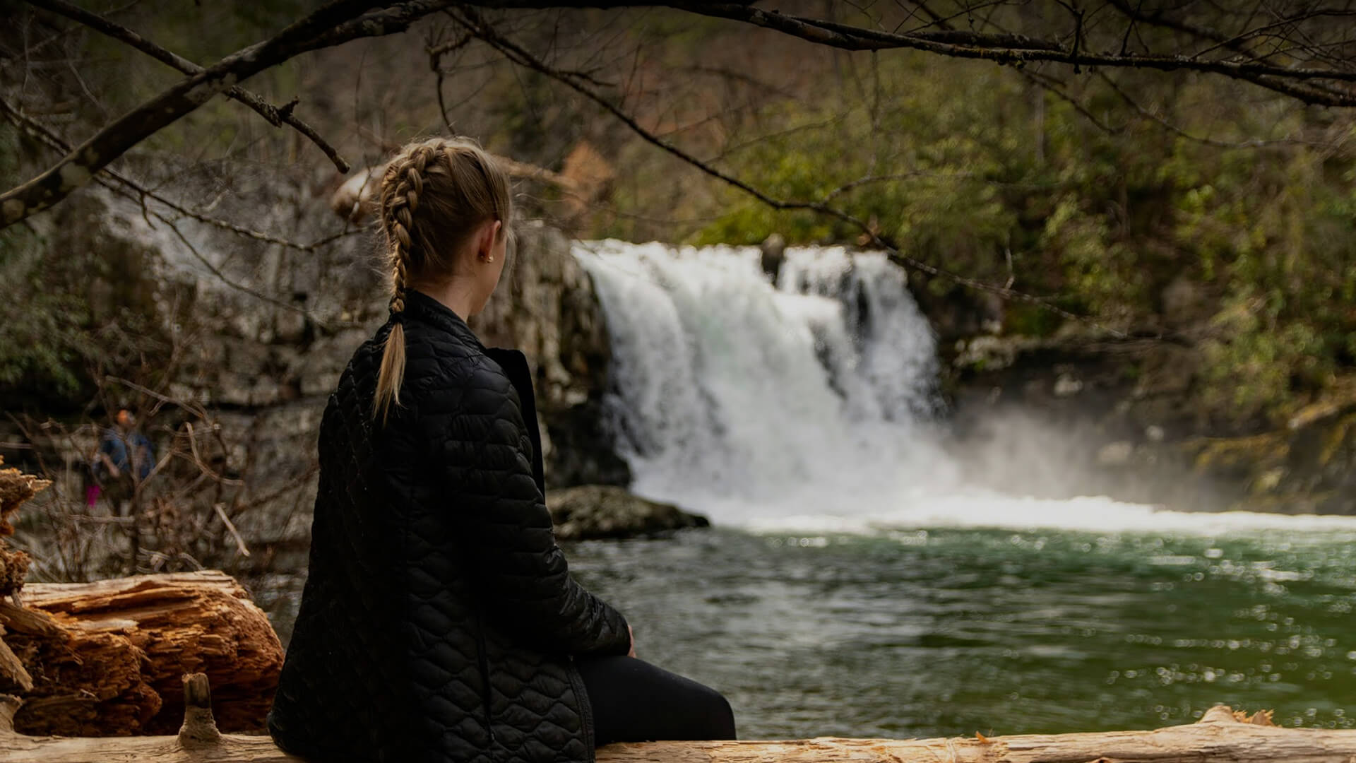 a woman sitting on a log by a waterfall