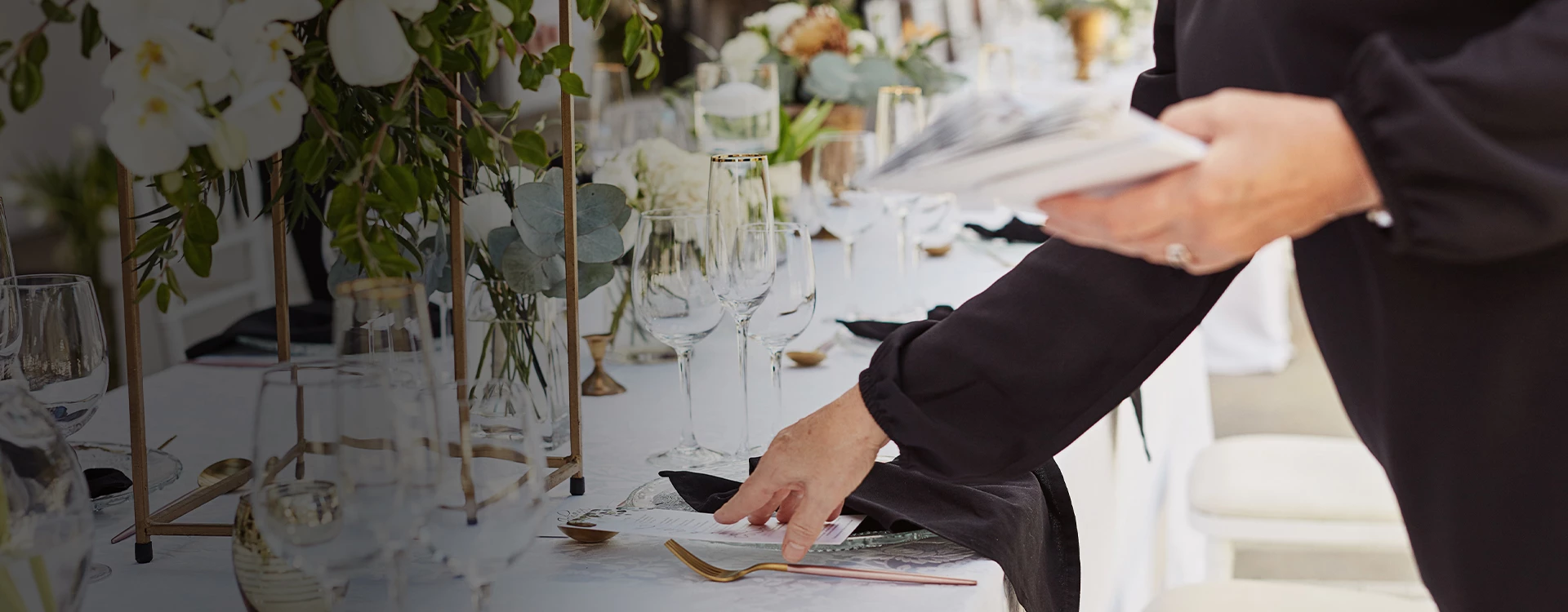 a person setting a table with white flowers and glasses