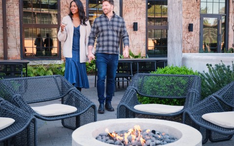 a man and woman holding hands and walking in front of a fire pit