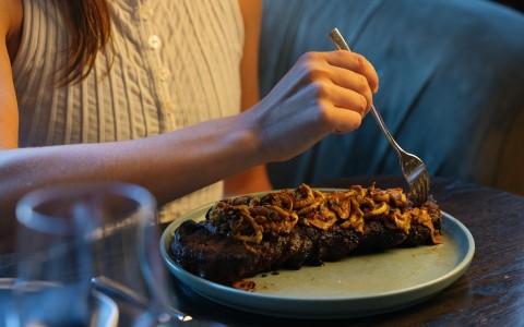 a person eating a steak with mushrooms on a plate